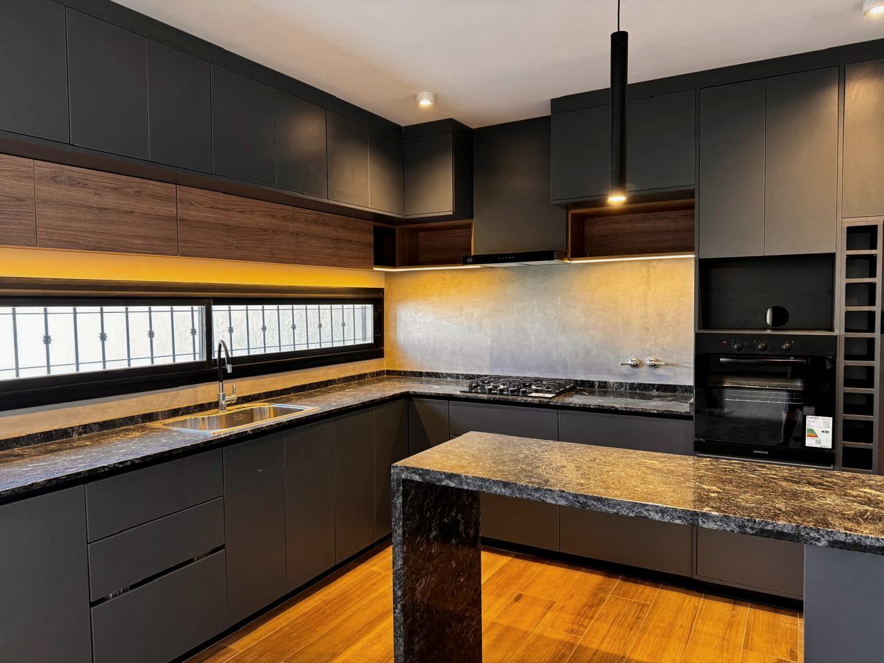 Cocina en negro con luz lineal cálida bajo las alacenas